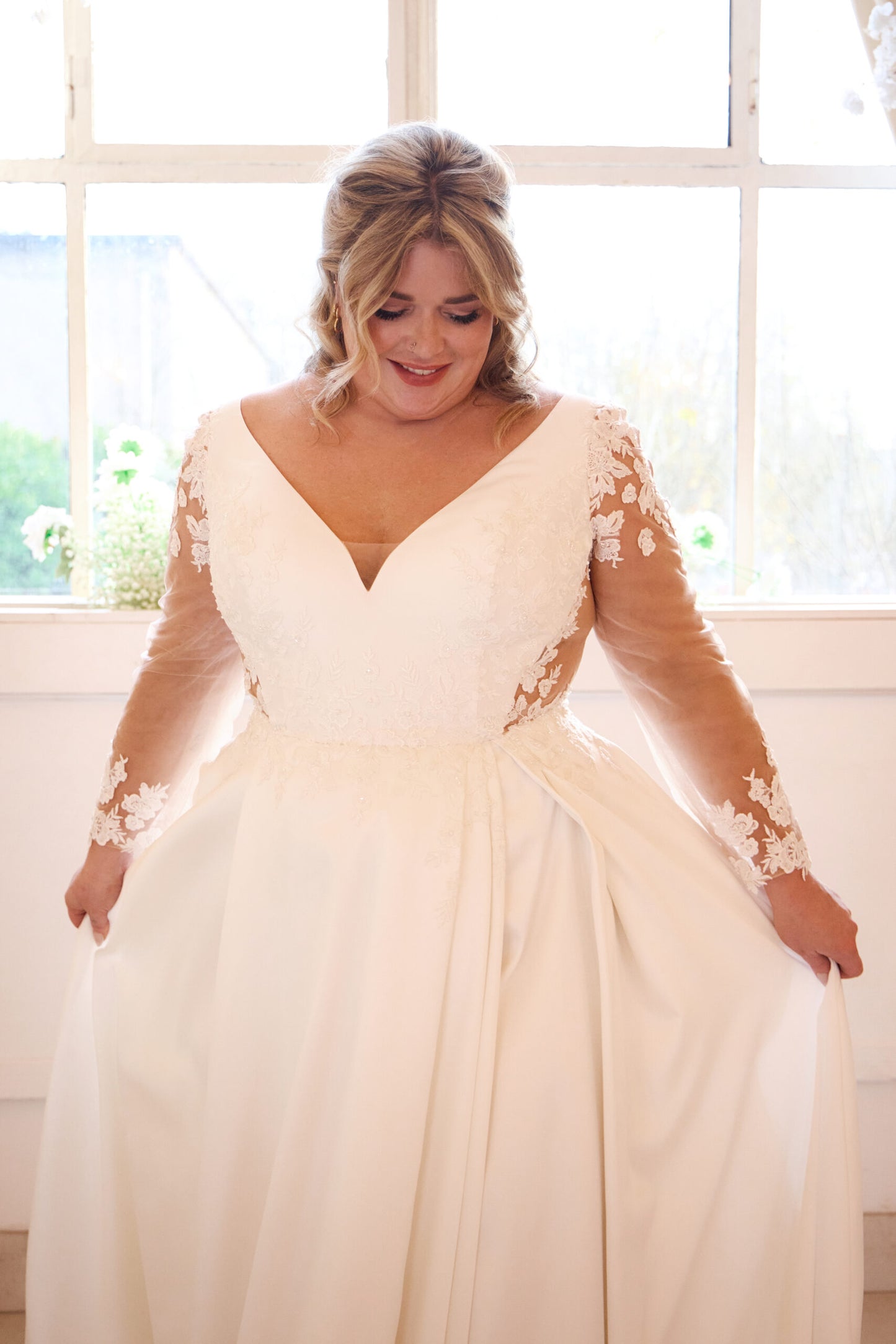 Curvy bride wearing long-sleeved wedding dress with satin A-line silhouette and deep neckline