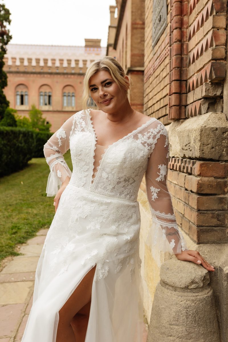 Elegant plus-size bridal gown with sheer lace sleeves, plunging neckline, and sweeping train
