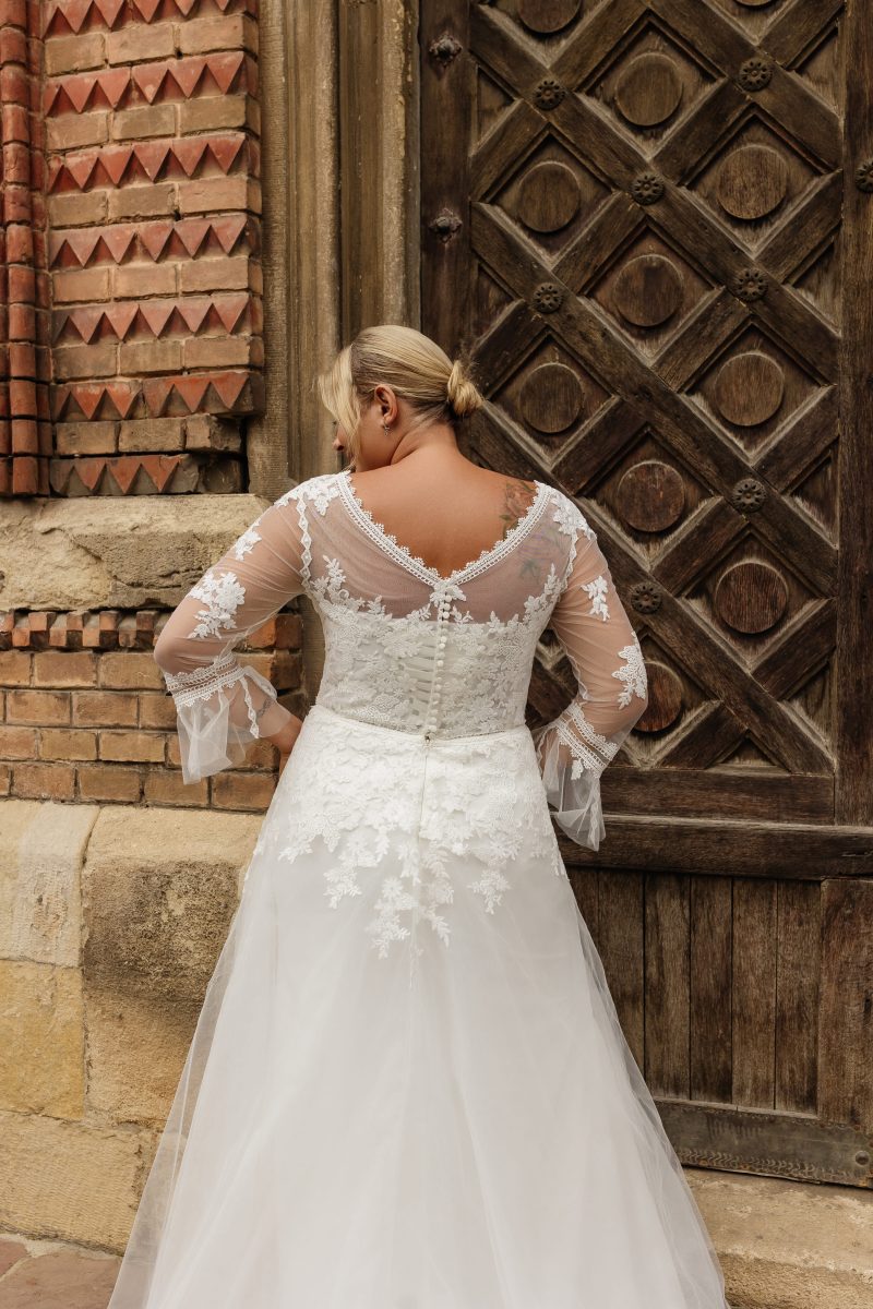 Plus-size wedding gown featuring V-neckline, long lace sleeves, and side slit for confident brides