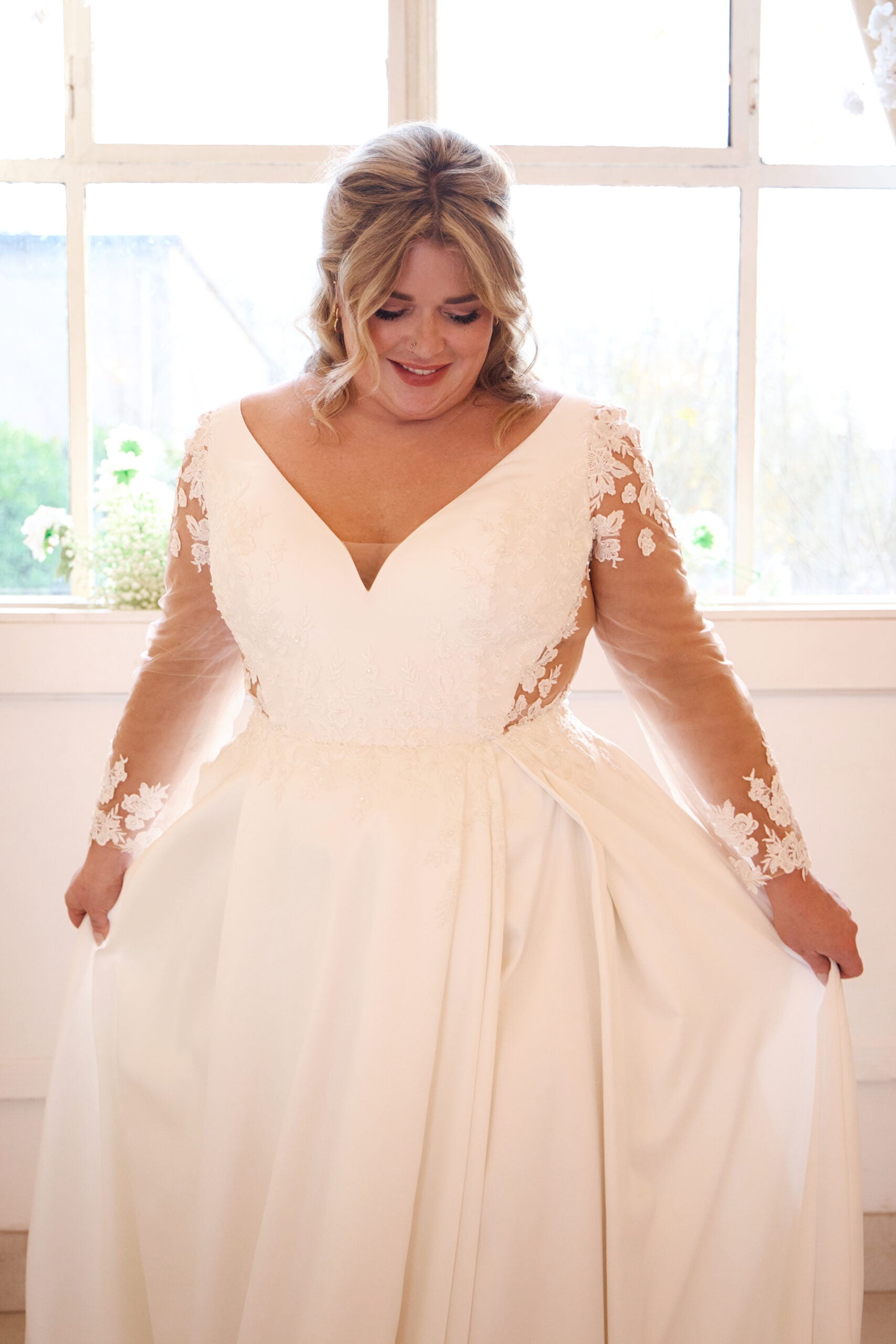 Curvy bride wearing long-sleeved wedding dress with satin A-line silhouette and deep neckline

