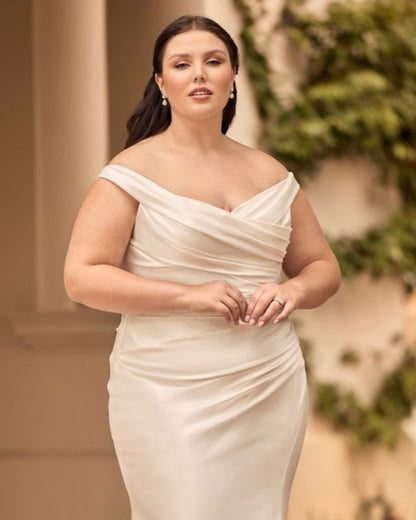 Plus-size bride wearing V-neck mermaid gown with sweeping train and off-shoulder satin drape

