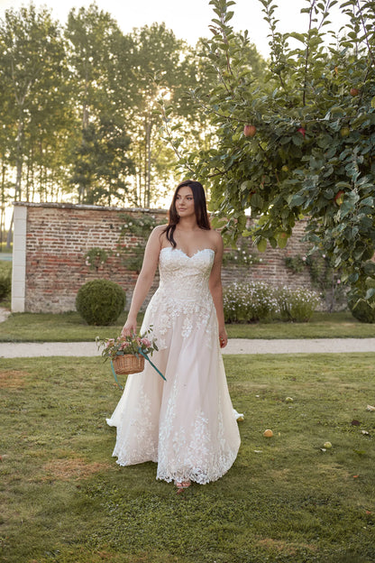Curvy bride in strapless A-line wedding dress walking through garden